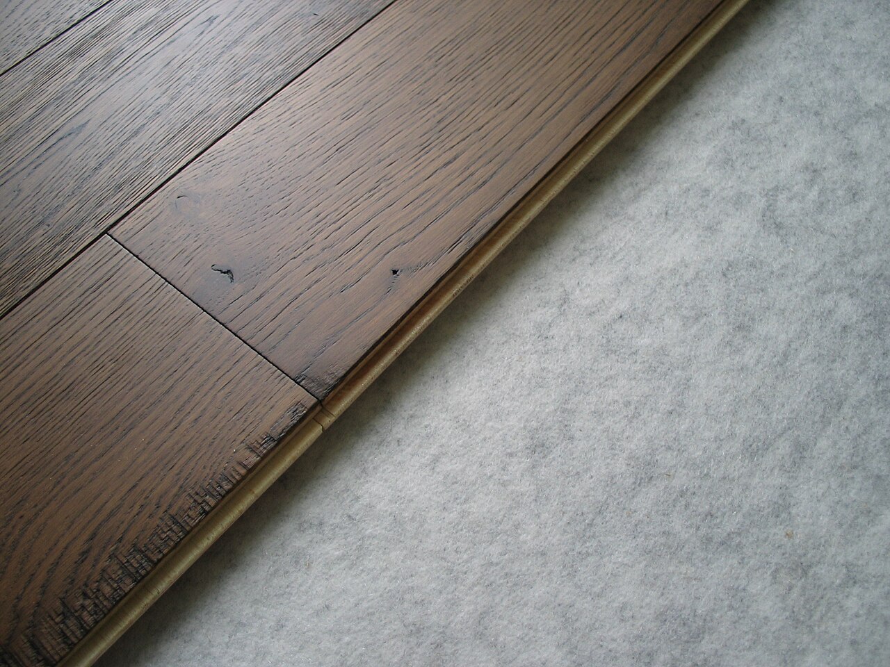 Photographie rapprochée du bord et de la languette d'une lame de parquet contrecollé posée sur une sous-couche